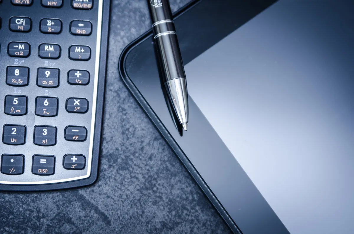 Calculadora financeira, caneta e tablet sobre mesa de pedra